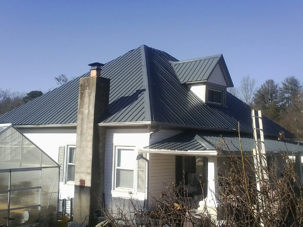 Dark blue standing seam metal roof on a white farmhouse with dormer — Slate & Tile Roof Repair by Roofing Brothers in Roswell