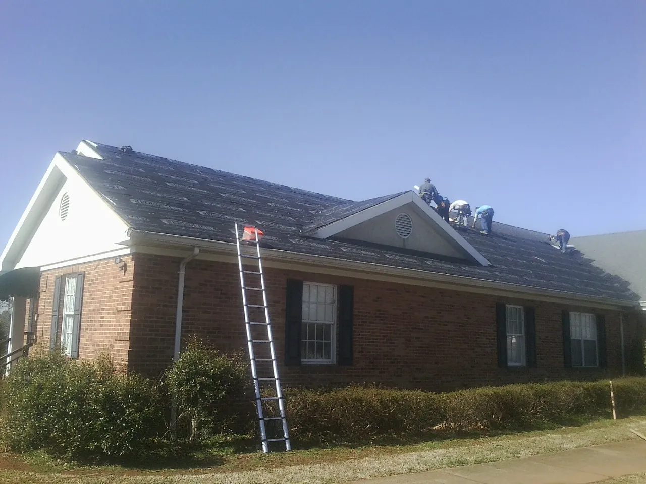 Crew tearing shingles off a brick ranch roof with a ladder set — Metal Roof Repair work by our crew in Roswell