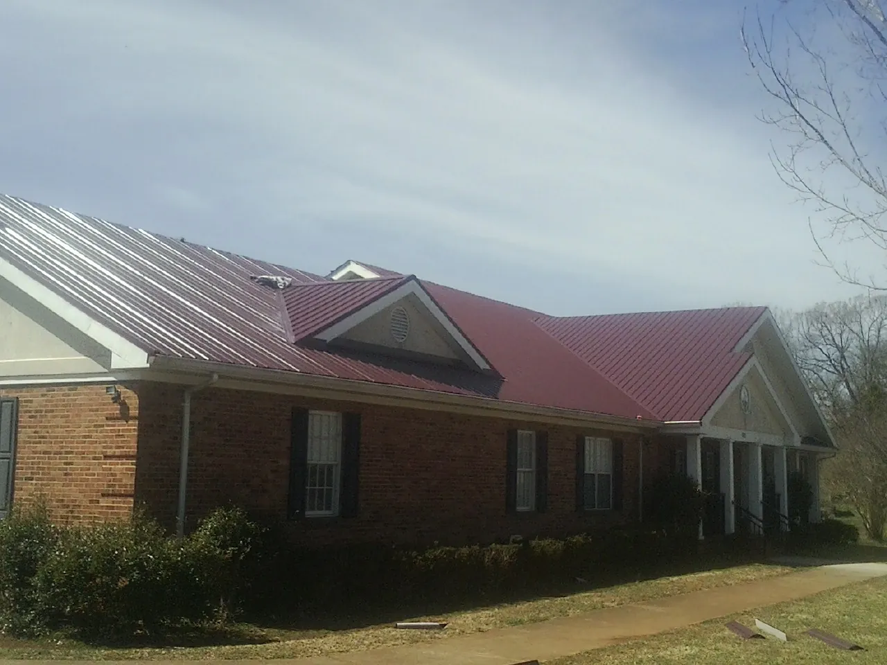 Red metal roof with gabled entries on a long brick building, from a Hail Damage Roof Repair job in Roswell