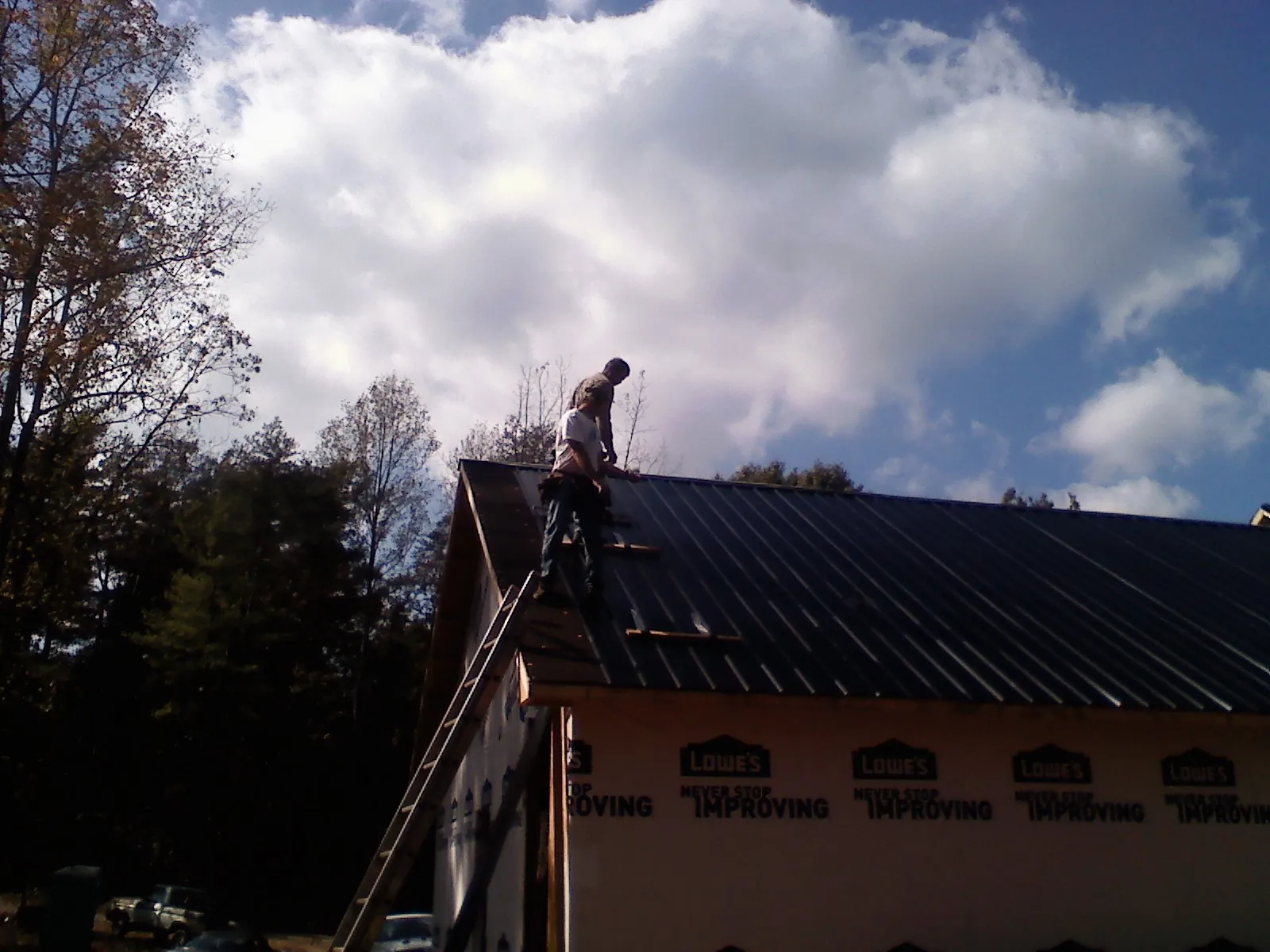 Roofer fastening dark metal panels high against a cloudy sky, from a Roof Inspection job in Roswell