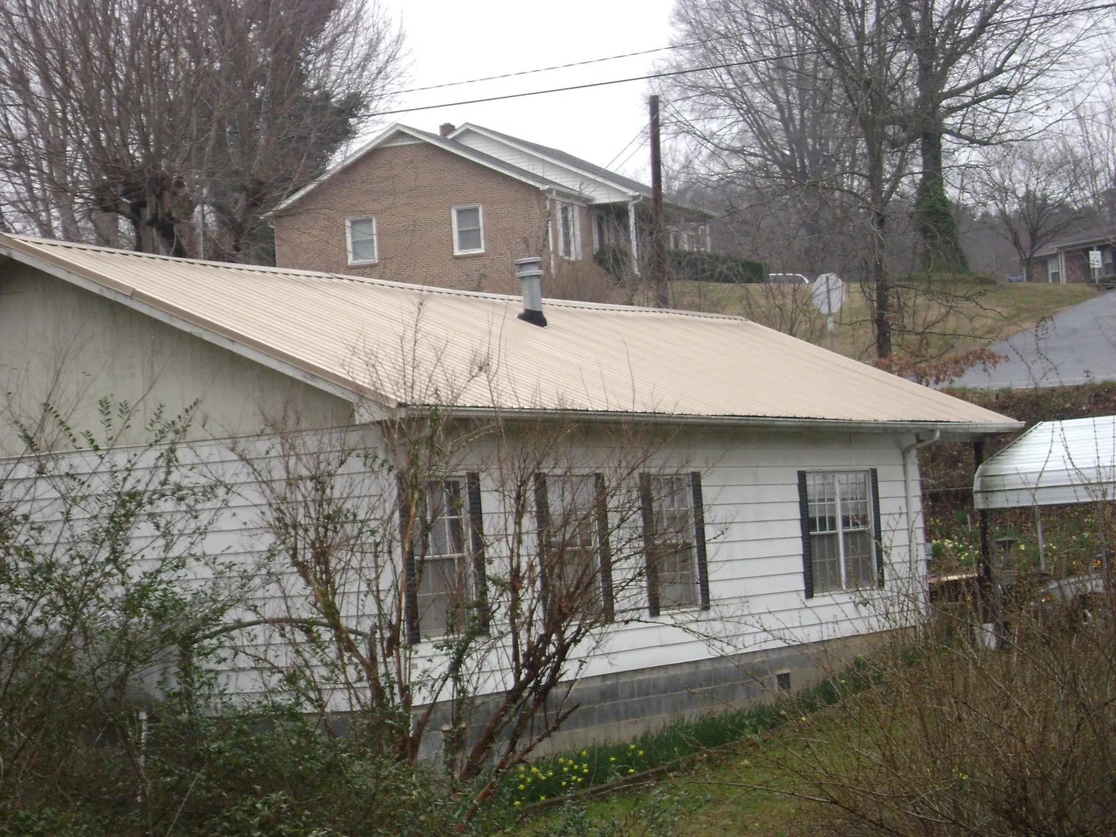 Tan metal roof on a white sided house set into a hillside — Commercial Roofing by Roofing Brothers in Roswell