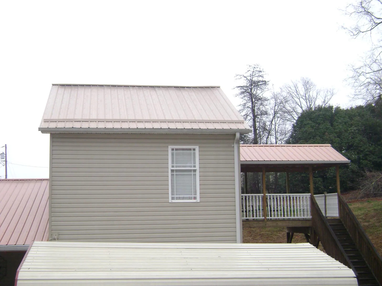 Tan metal roofs on a two story addition and attached porch, from a Roof Replacement job in Roswell
